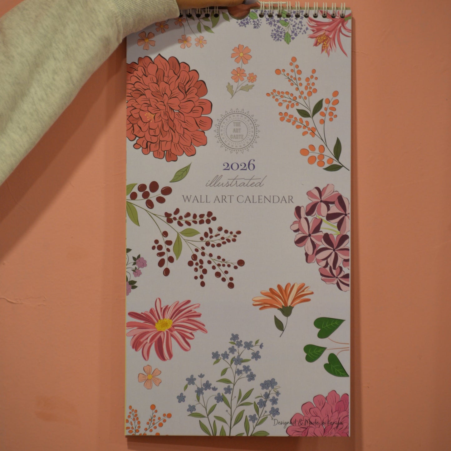 Floral wall calendar held against a peach-colored wall