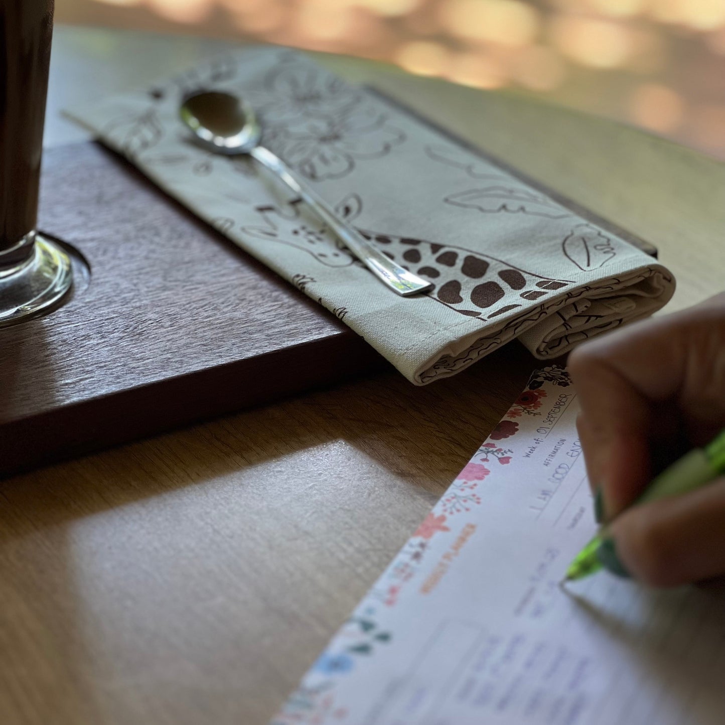 Person writing on a menu with a glass of coffee and spoon on a table