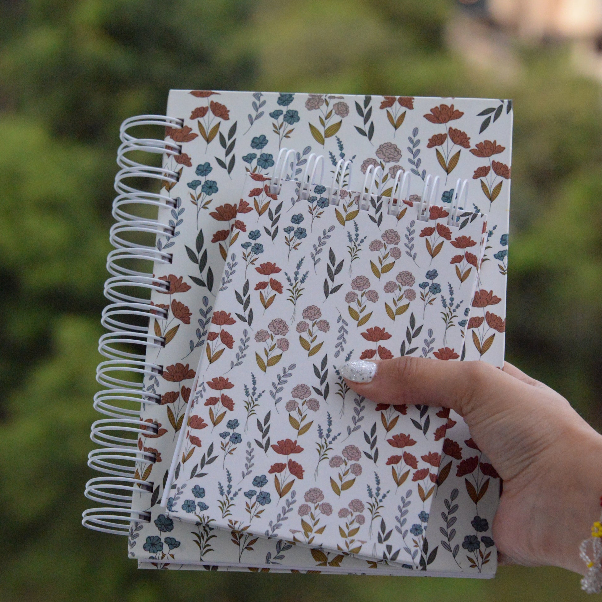 Notebook with floral pattern held by a hand against a blurred green background