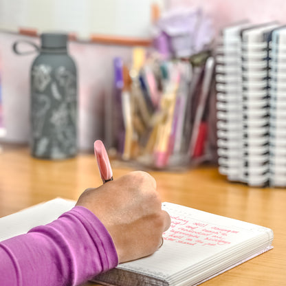 Person writing in a notebook with stationery items in the background