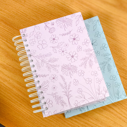 Two spiral-bound notebooks with floral patterns on a wooden surface
