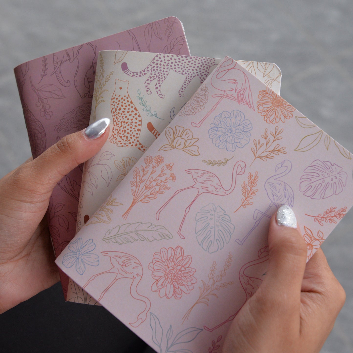 Three patterned notebooks held by a person against a neutral background