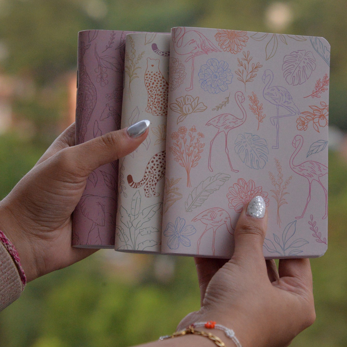 Two patterned books held by a person with a blurred natural background
