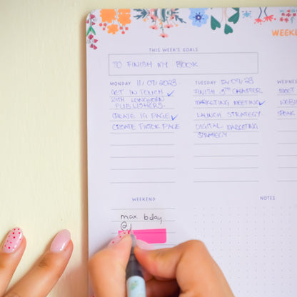 Person writing in a planner with a floral design on a light background