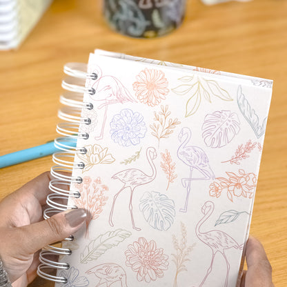 Notebook with floral and bird design held by a person on a wooden surface.