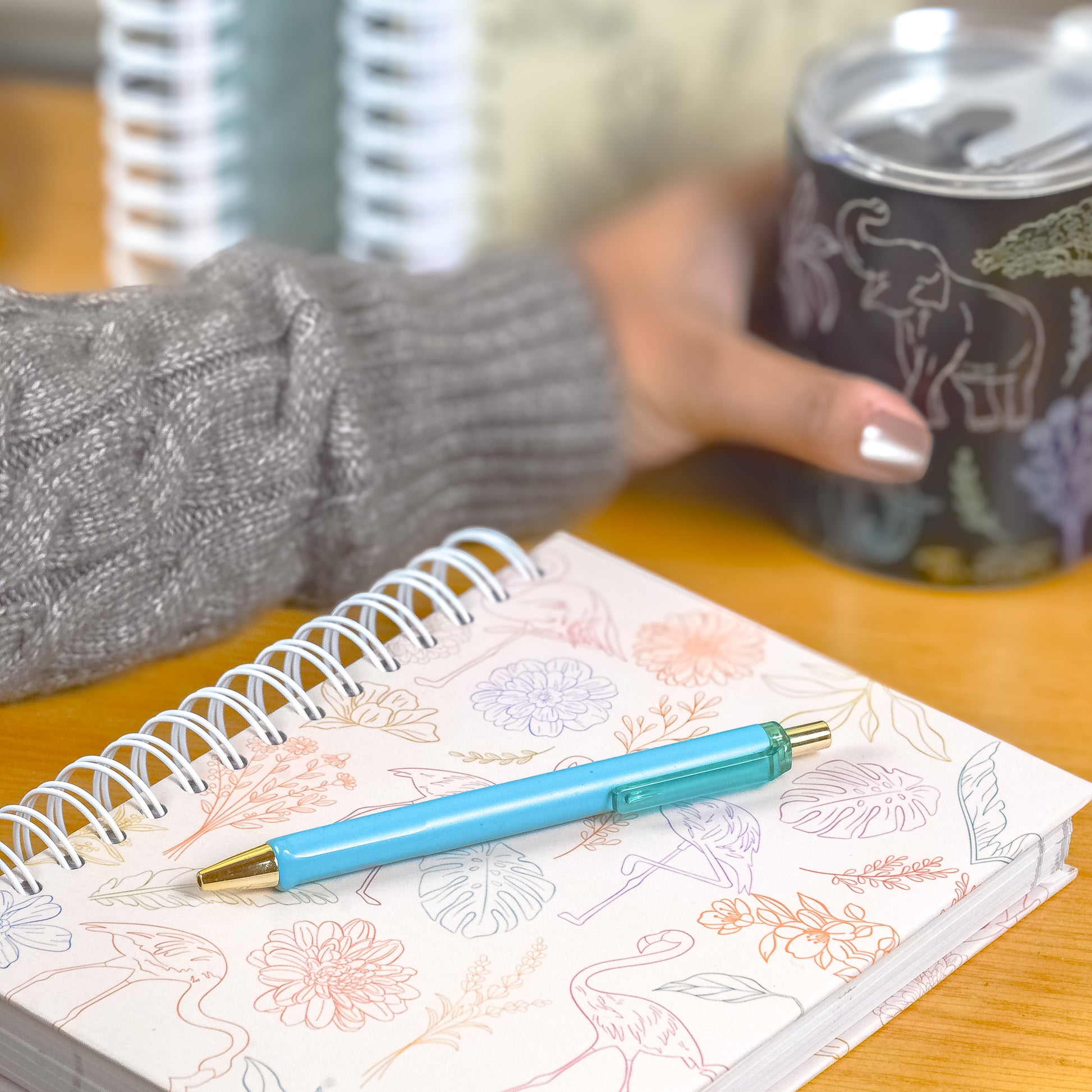 Person holding a mug with a notebook and pen on a wooden surface