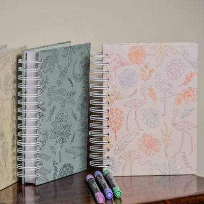 Three spiral-bound notebooks with floral patterns on a wooden surface.