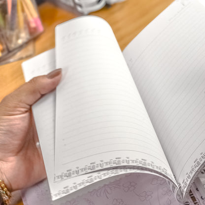 Hand holding an open notebook with decorative edges on a wooden surface.