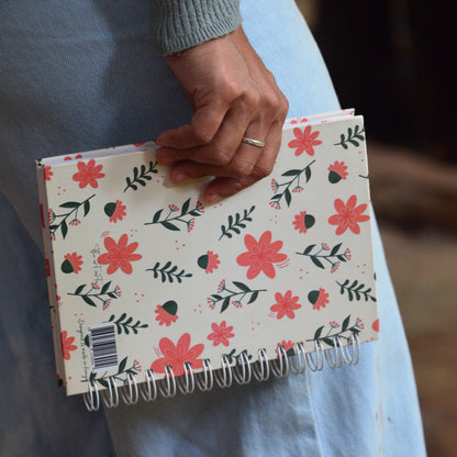 Notebook with floral design held by a person wearing a gray sweater.