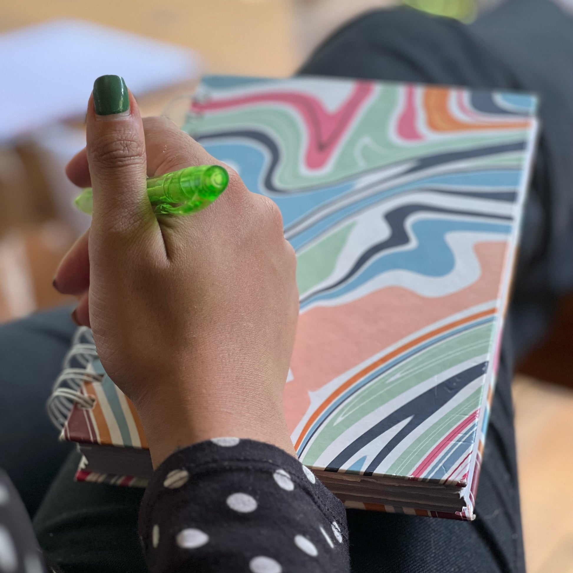 Hand holding a green marker with a colorful notebook in the background