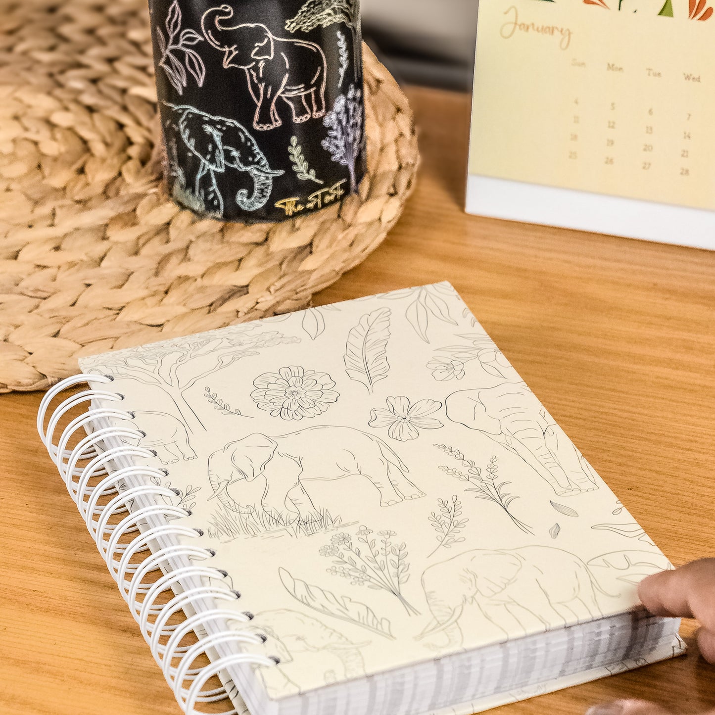 Notebook with animal illustrations on a wooden surface next to a mug and calendar.