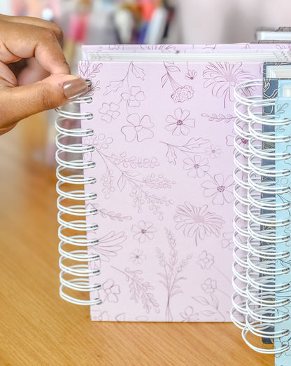 Hand holding a spiral-bound notebook with floral design on a wooden surface.